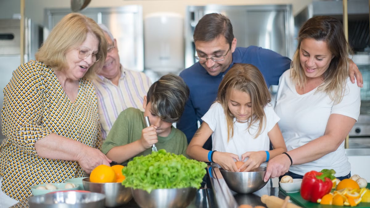 Family of various ages gathers in kitchen to cook meal together, showcasing culinary togetherness.